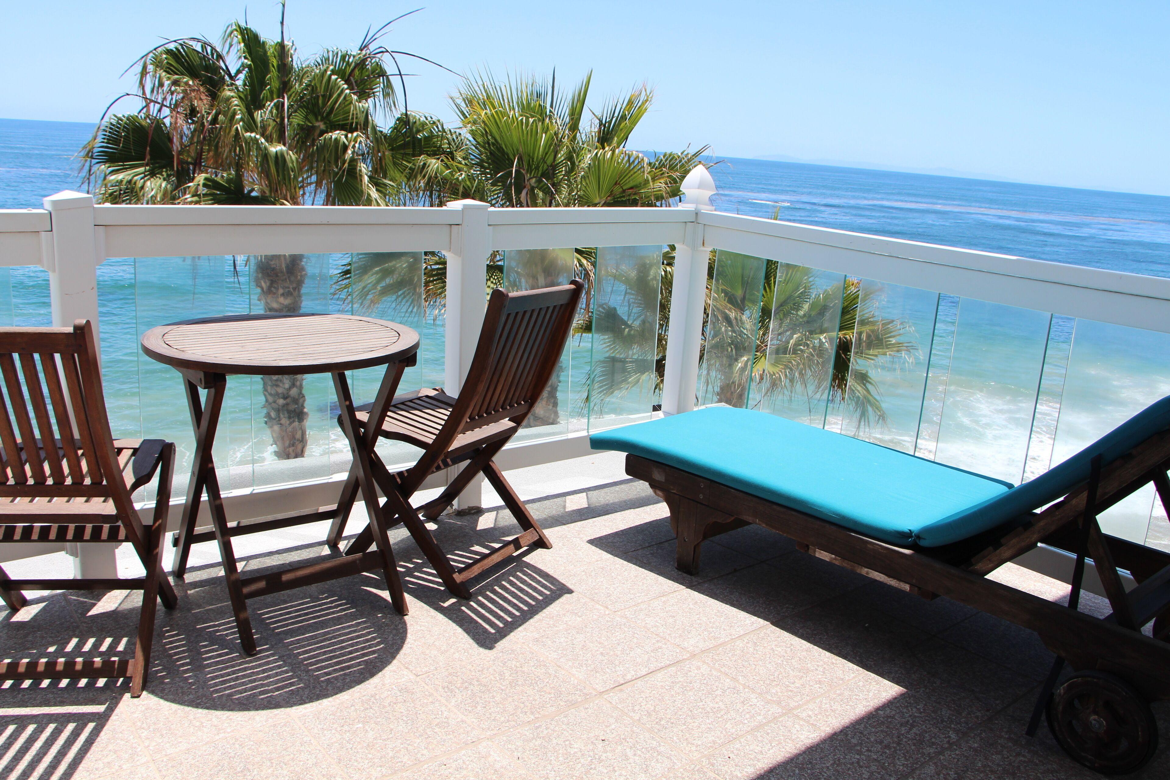 A balcony with a table and chairs, a lounge chair, and a view of the ocean.