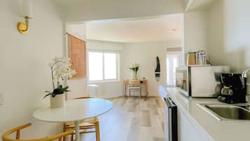 A modern kitchen with a white countertop, a sink, and a coffee maker. There is a dining area with a round table and wooden chairs.