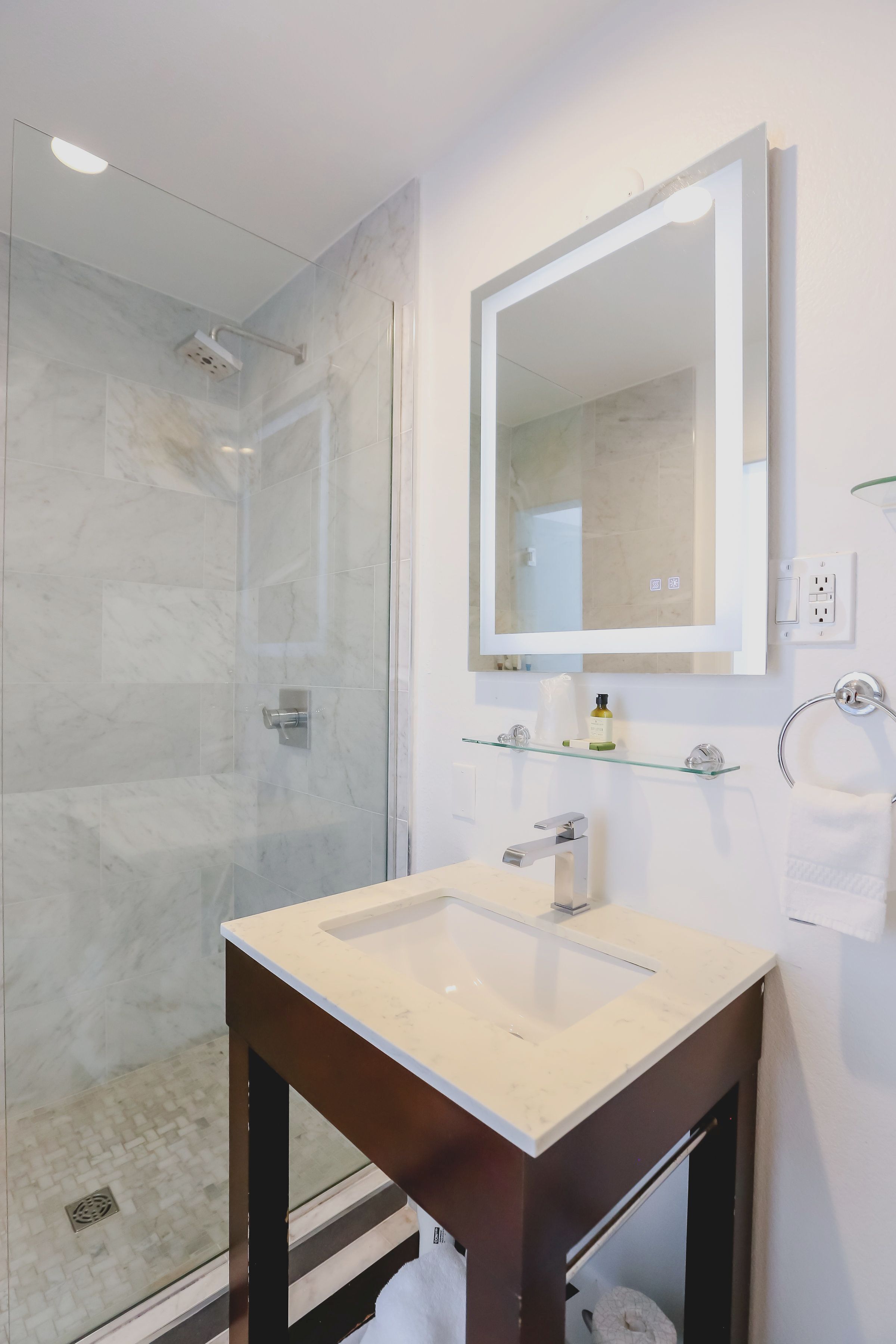 Un baño moderno con cabina de ducha de vidrio, un espejo grande y un tocador con lavabo.