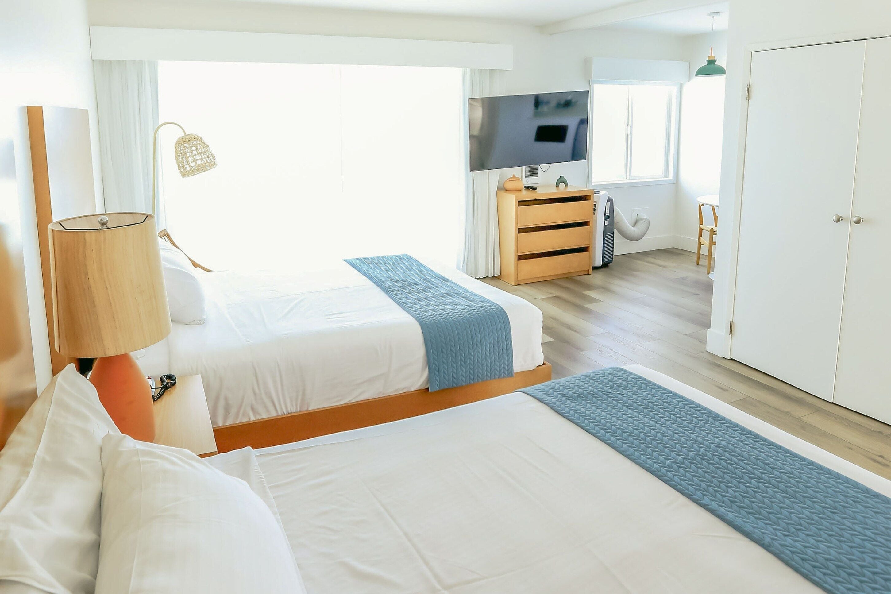 A hotel room with two beds, a TV, a wardrobe, and a desk with a lamp.