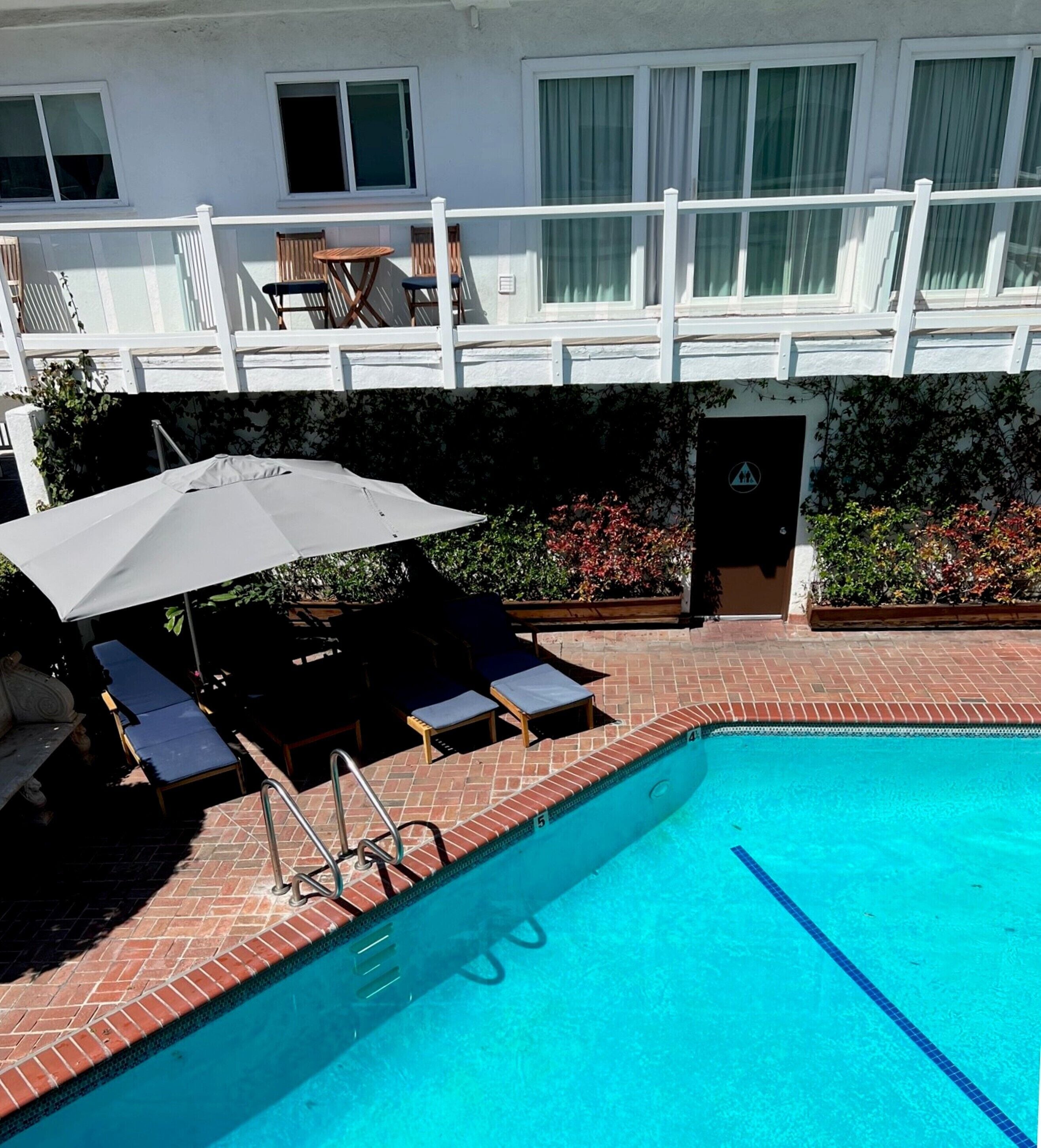 A swimming pool with a white umbrella, lounge chairs, and a brick border.