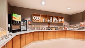 Un área de desayuno de hotel moderna, con una máquina de café de servicio propio, diversas opciones de comida y una distribución limpia y ordenada.