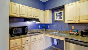 A modern kitchen with wooden cabinets, granite countertops, a microwave, coffee maker, sink, and dishwasher.