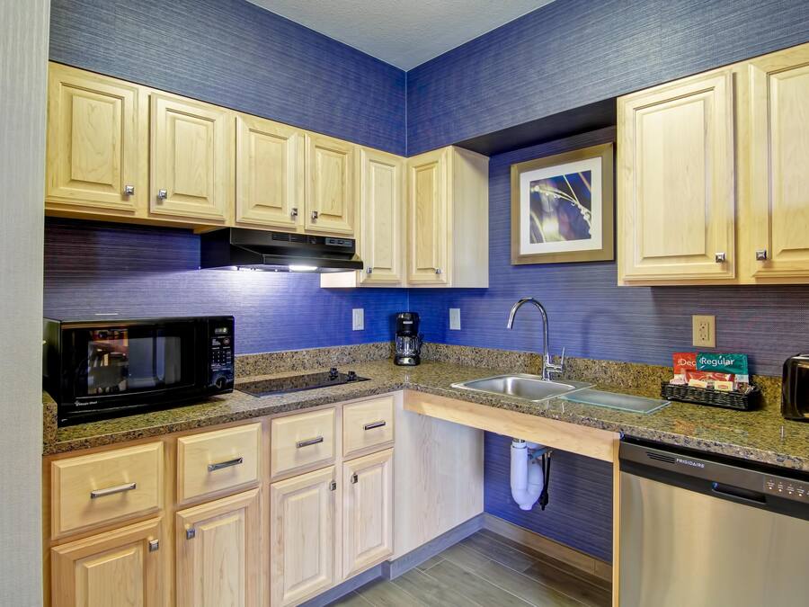 A modern kitchen with wooden cabinets, granite countertops, a microwave, coffee maker, sink, and dishwasher.