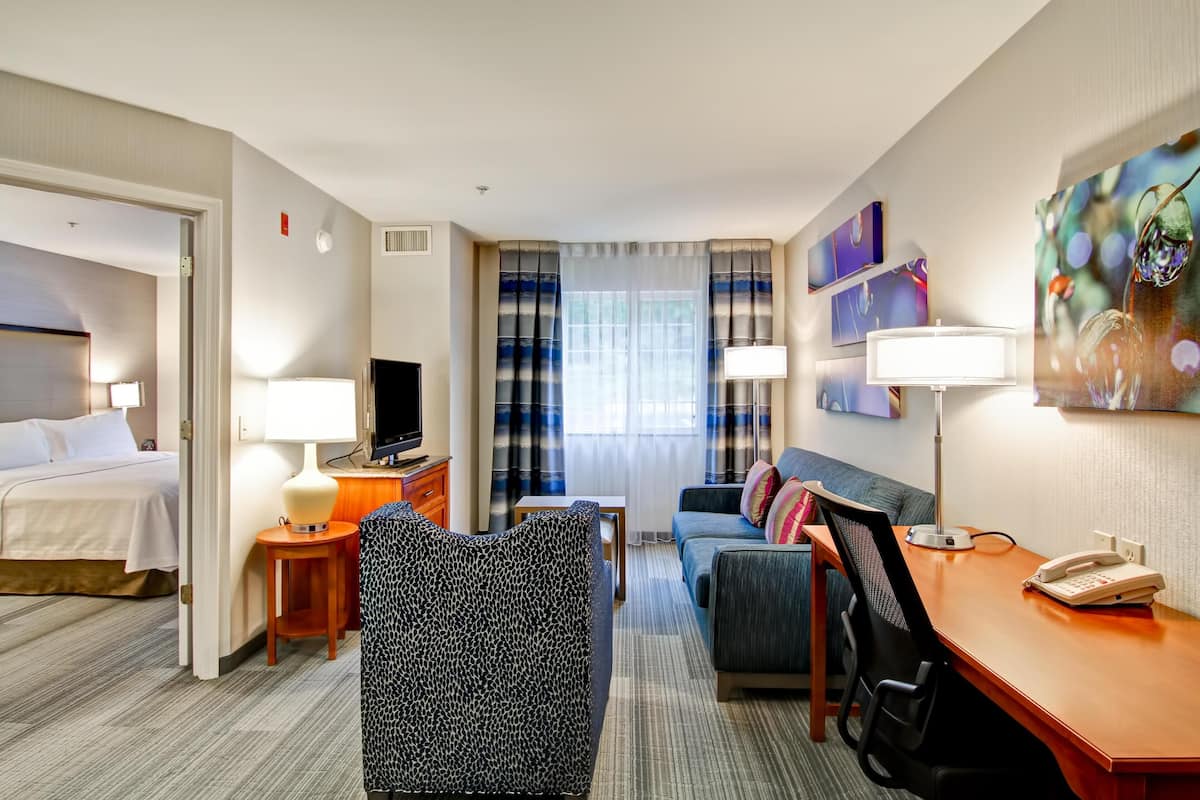 Ein Hotelzimmer mit Bett, Schreibtisch, Sofa, Fernseher und Kunstwerken an den Wänden.