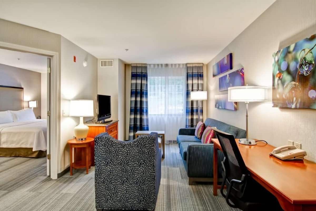Ein Hotelzimmer mit Bett, Schreibtisch, einer Sitzecke, einem Fernseher und einem Bild an der Wand.
