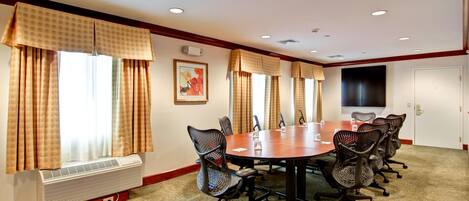 A conference room with a large table, black mesh chairs, and a flat-screen TV on the wall.