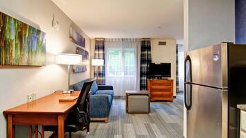 A compact hotel room with a kitchenette, a sofa, a desk, and a TV.