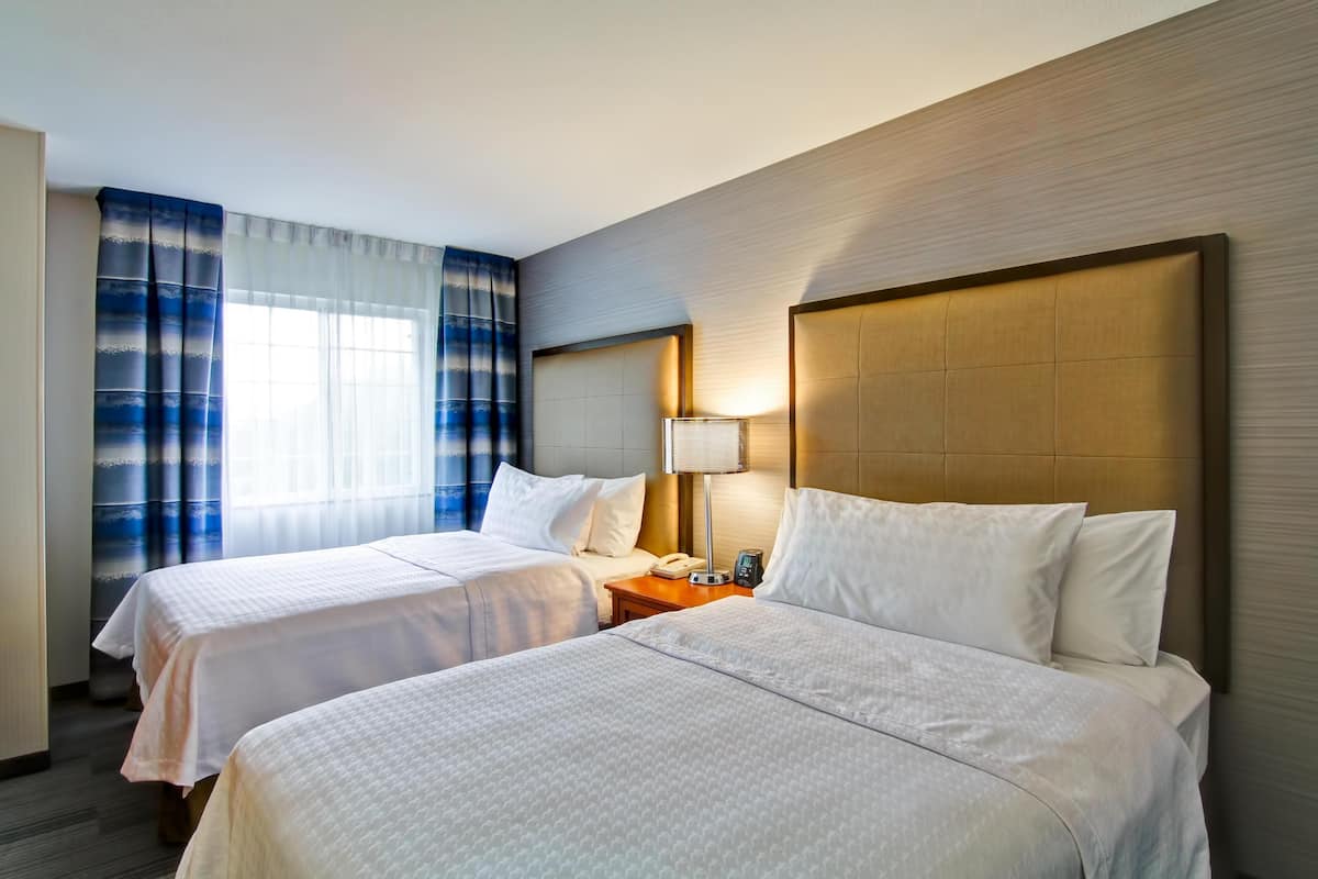 Ein Hotelzimmer mit zwei Betten, einem Nachttisch, einer Lampe und einem Fenster mit Vorhängen.