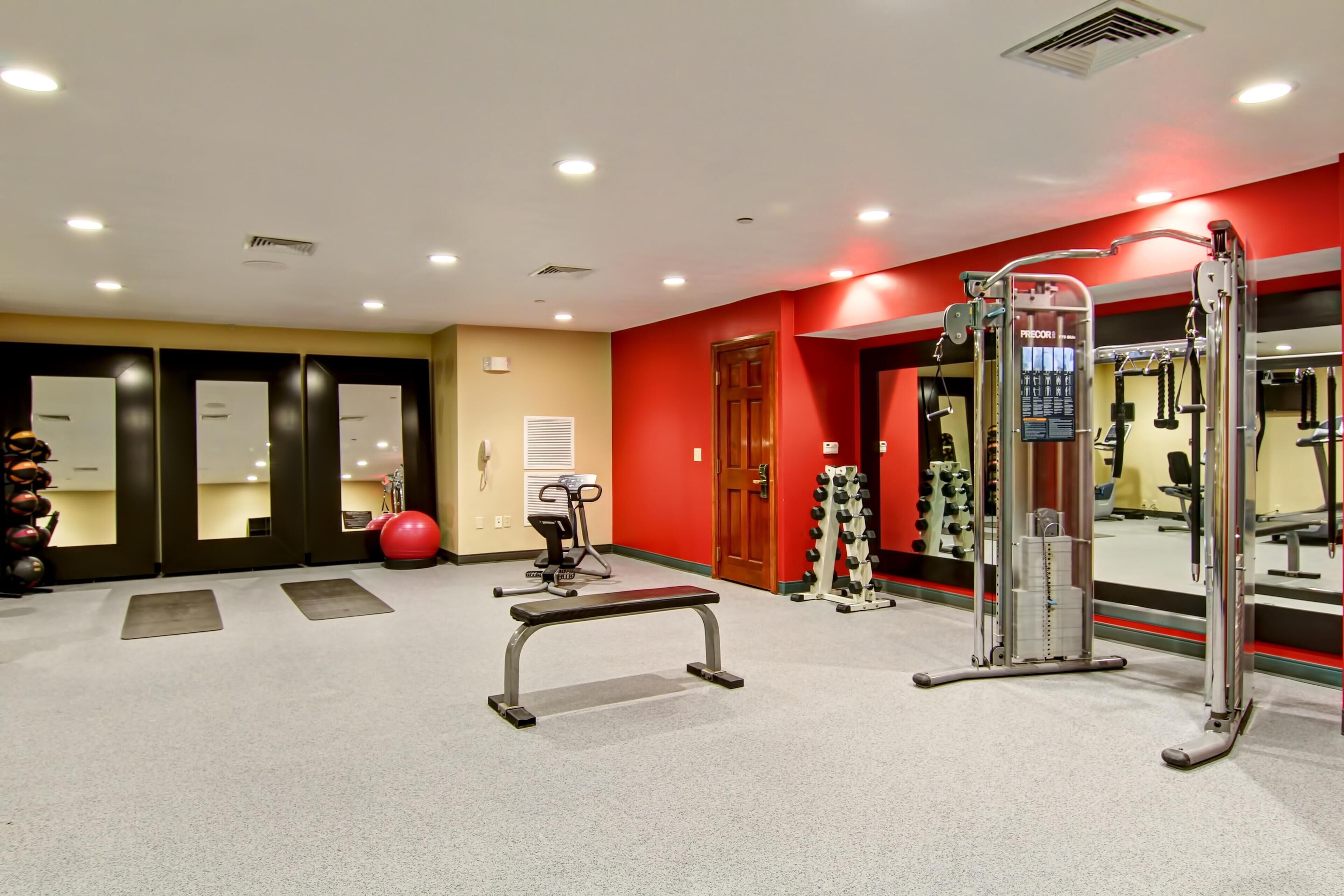 A gym with exercise equipment, a bench, and a red wall.