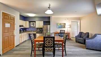 A modern kitchen with wooden cabinets, a dining table with patterned chairs, and a living area with a sofa and armchair.