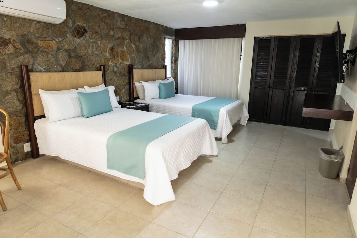 A hotel room with two beds, a stone wall, a window with curtains, a wardrobe, and a trash bin.