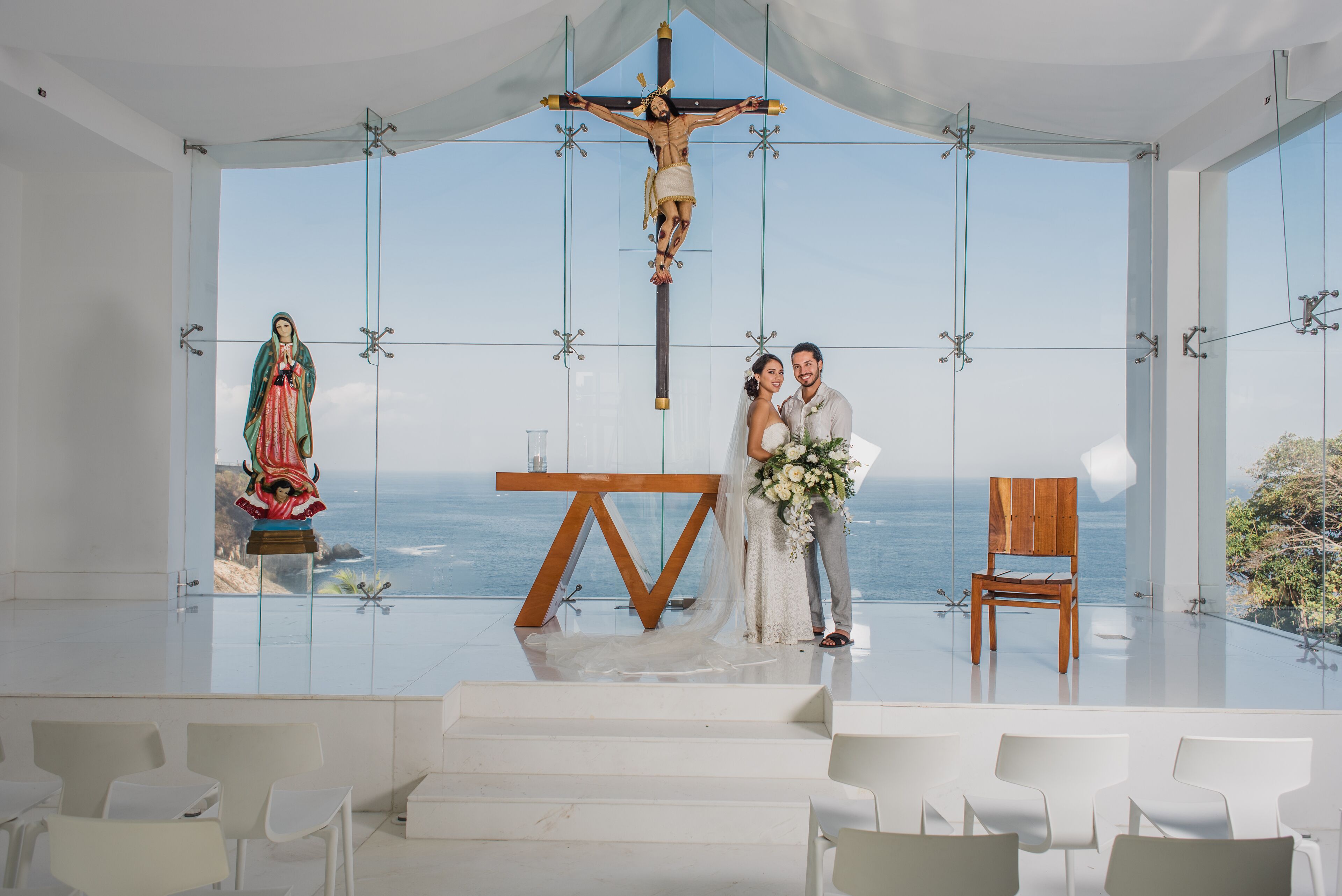 A wedding ceremony with a view of the ocean, a crucifix, and a statue of the Virgin Mary.
