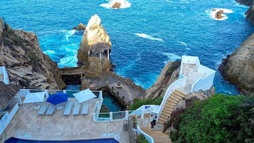 Um hotel à beira-mar com piscina, uma escadaria que leva até a falésia e vista para o mar.
