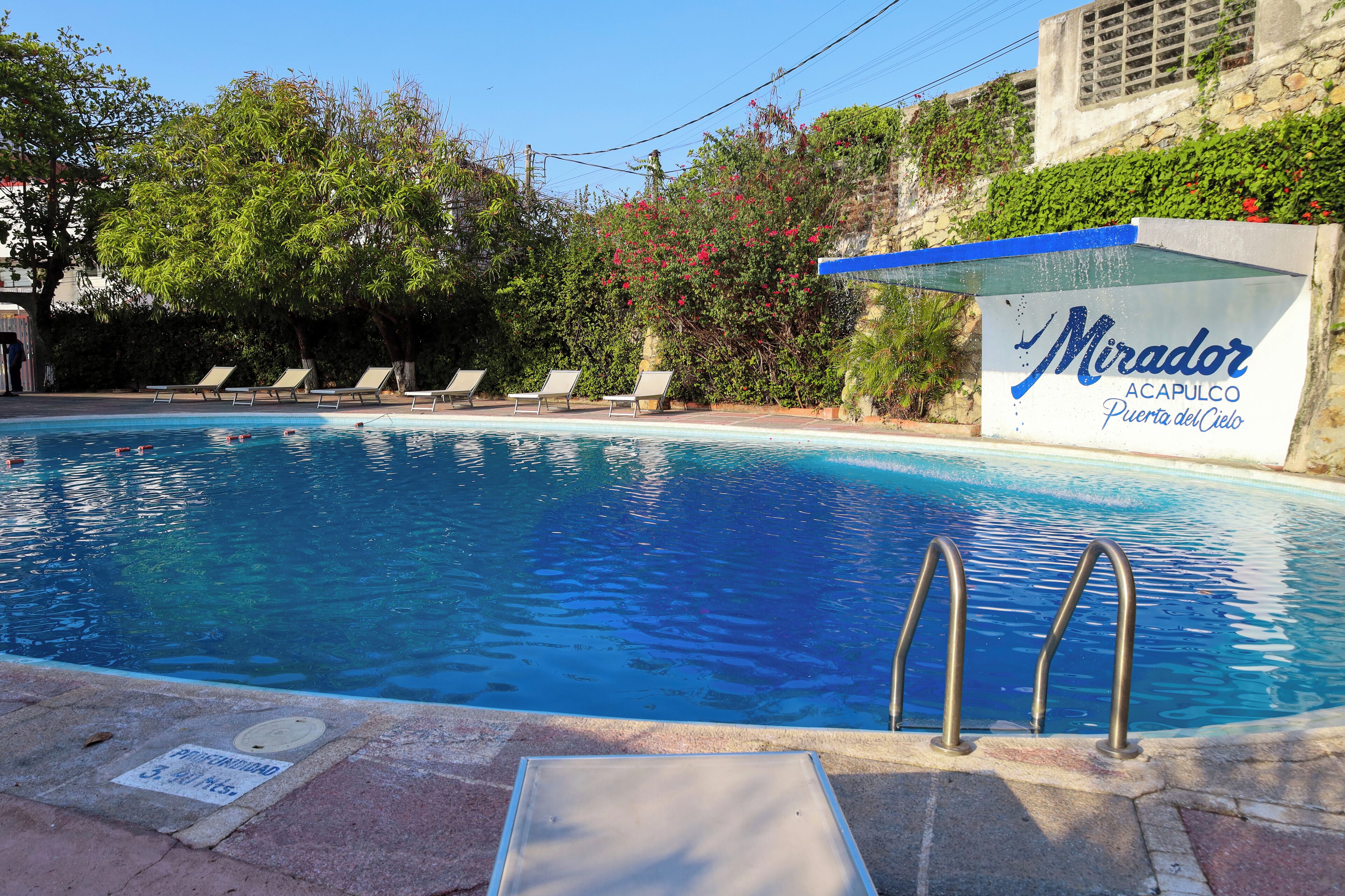 Una piscina con sillas de descanso y un cartel que dice 'Mirador Acapulco Puerta del Cielo'.