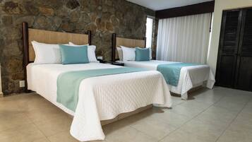 A hotel room with two beds, stone walls, a tiled floor, and a window with curtains.