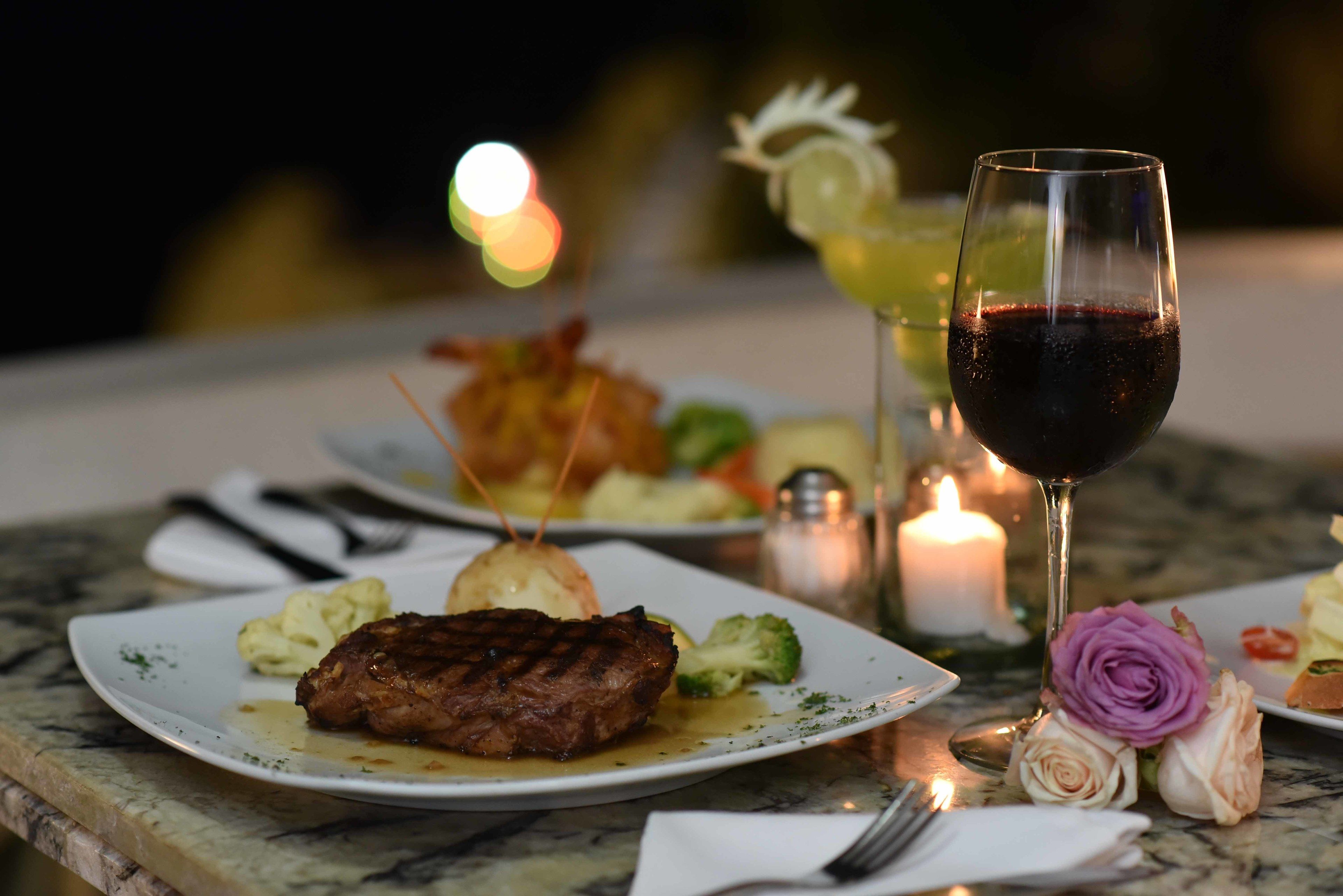 Una mesa con un plato de comida, una copa de vino tinto y una vela.