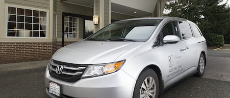 A silver Honda minivan parked in front of a building with a brick facade and large windows.