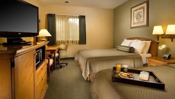 A hotel room with two beds, a desk with a computer, a television, and a tray with breakfast items.