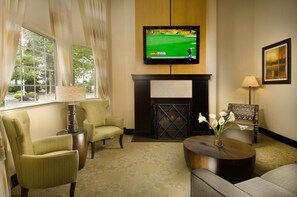 A room with a fireplace, a television mounted above it, and two armchairs.