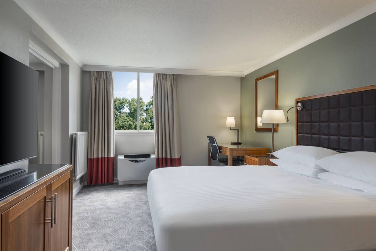 A hotel room with a large bed, a desk with a chair, a television, and a window with curtains.