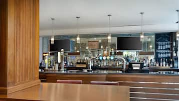 Zona de bar con muebles de madera, una barra y lámparas colgantes.