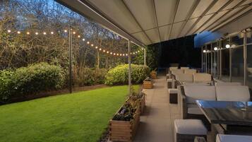 An outdoor patio area with wicker furniture, string lights, and planters along a pathway.
