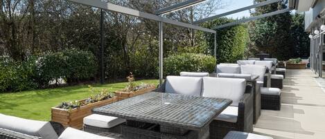 Eine Terrassengruppe mit Korbmöbeln, einem Holztisch und einer Pergola.