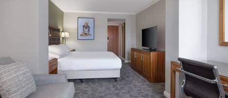 Habitación de hotel con una cama, un escritorio con silla, un televisor y un cuadro en la pared.