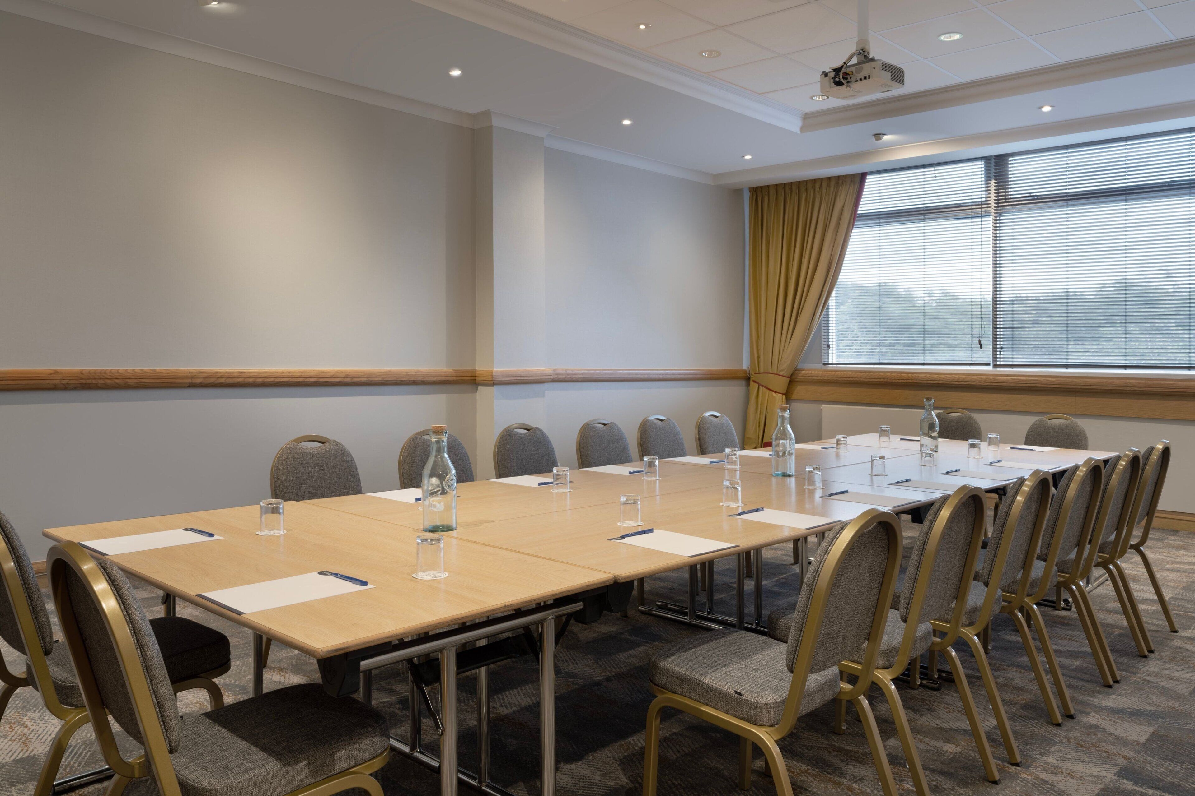 A conference room with a long table, chairs, and a projector on the ceiling.