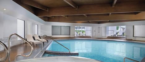 An indoor swimming pool with a hot tub, lounge chairs, and a view of the outdoors.
