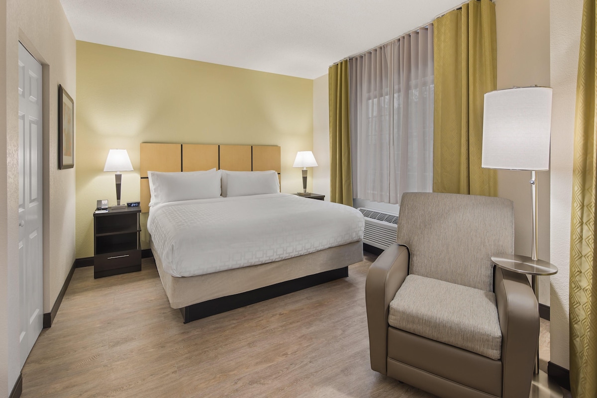 Een hotelkamer met een groot bed, twee nachtkastjes met lampen, een stoel en een raam met gordijnen.