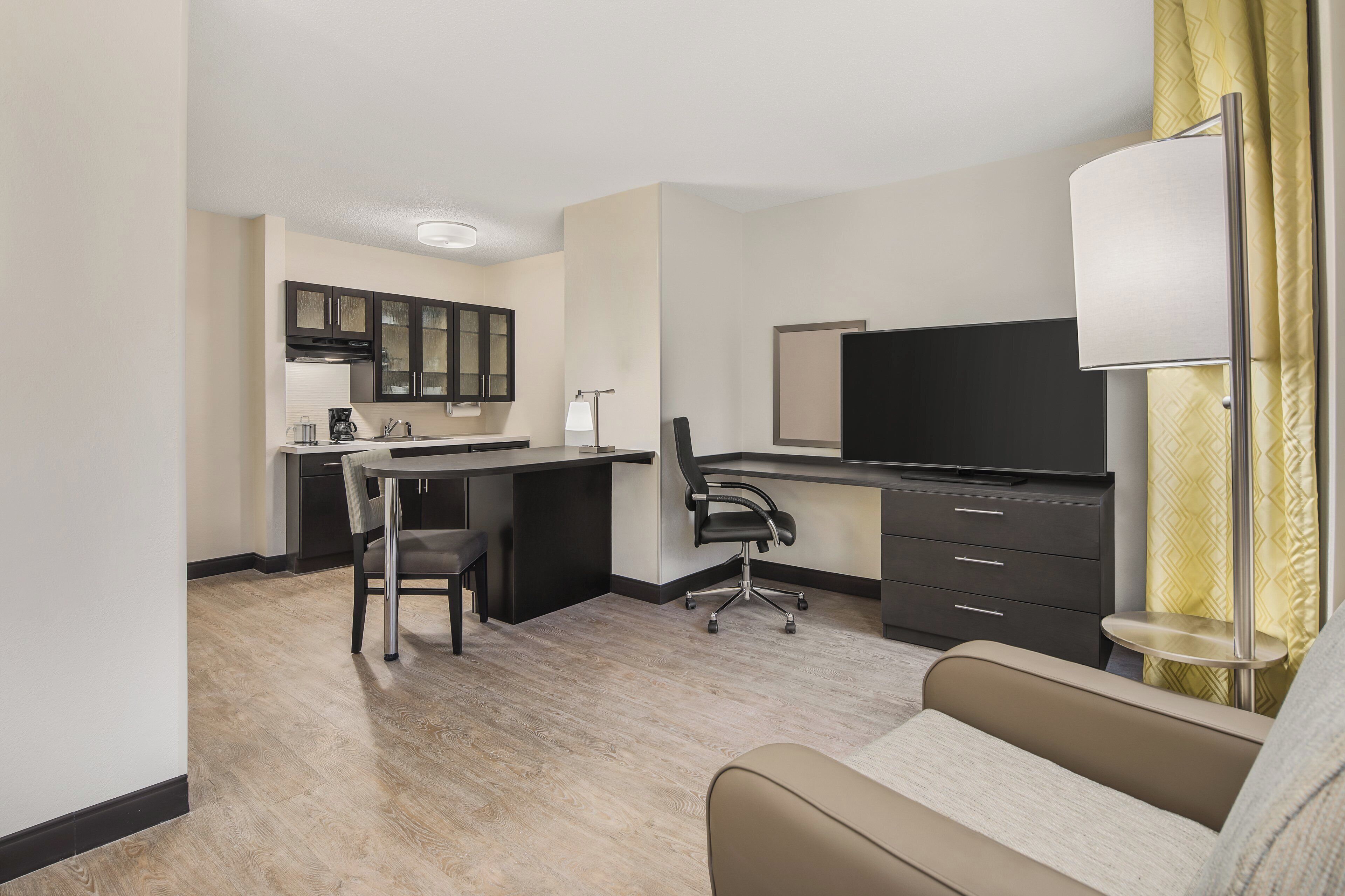 Quarto de hotel com cama, escrivaninha, cadeira, televisão e abajur.
