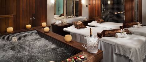 A spa room with a hot tub, towels, and a tray of fruit.