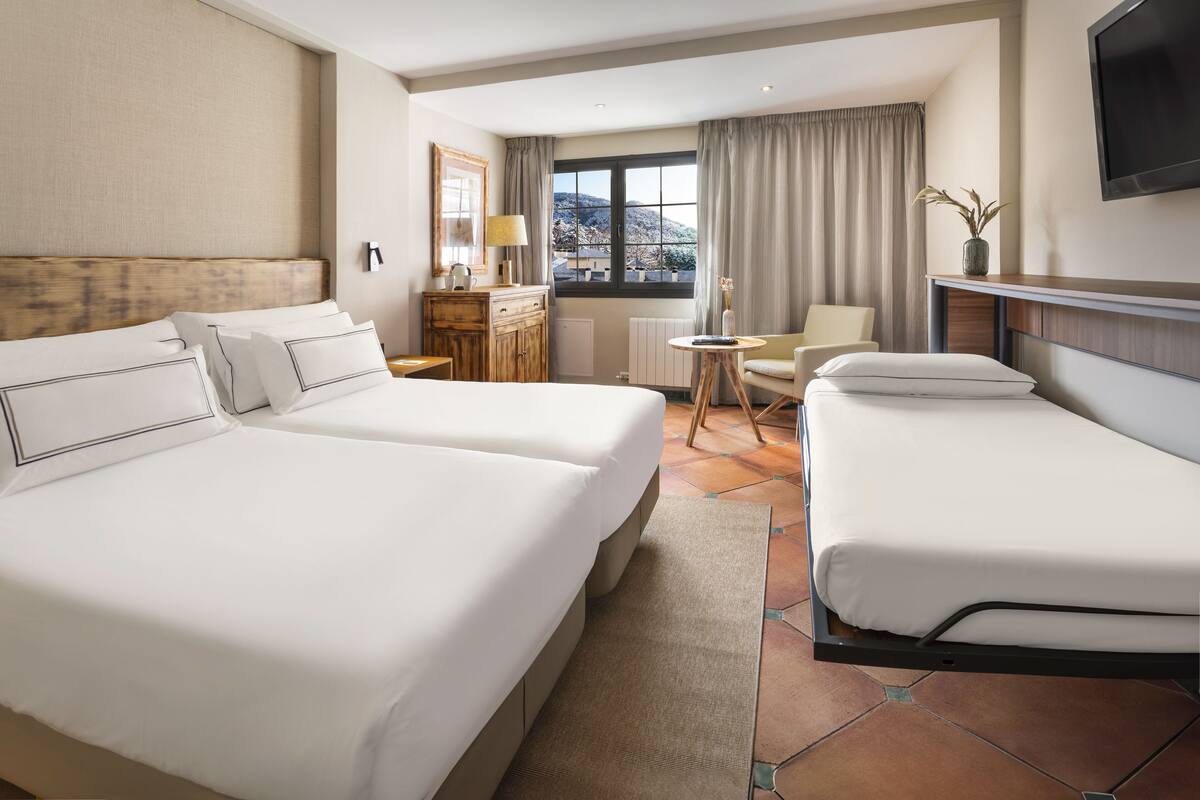 Una habitación de hotel con dos camas, un escritorio, una silla, un televisor y una ventana con cortinas.