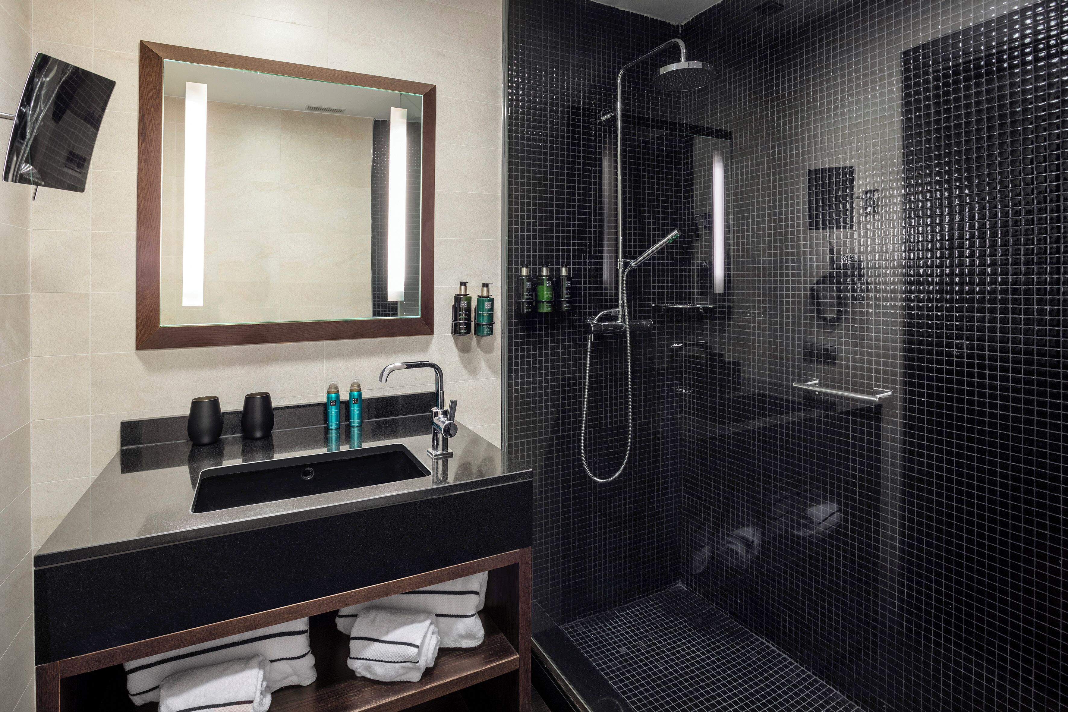 A modern bathroom with a large mirror, a black sink, and a shower enclosure.