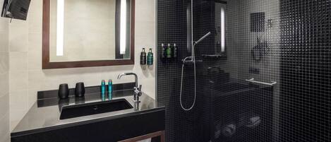 A modern bathroom with a large mirror, a black sink, and a shower enclosure.