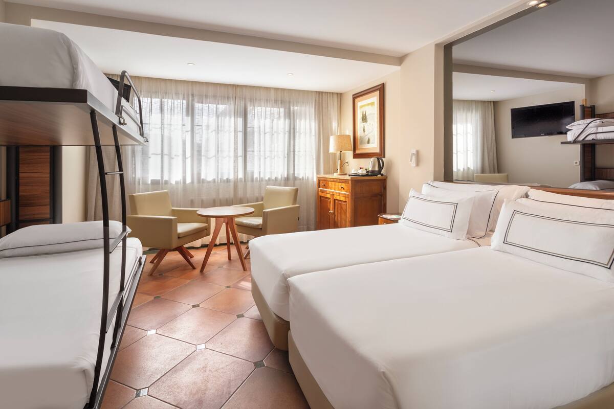Habitación de hotel con dos camas, un escritorio, una silla, un televisor y una ventana con cortinas.