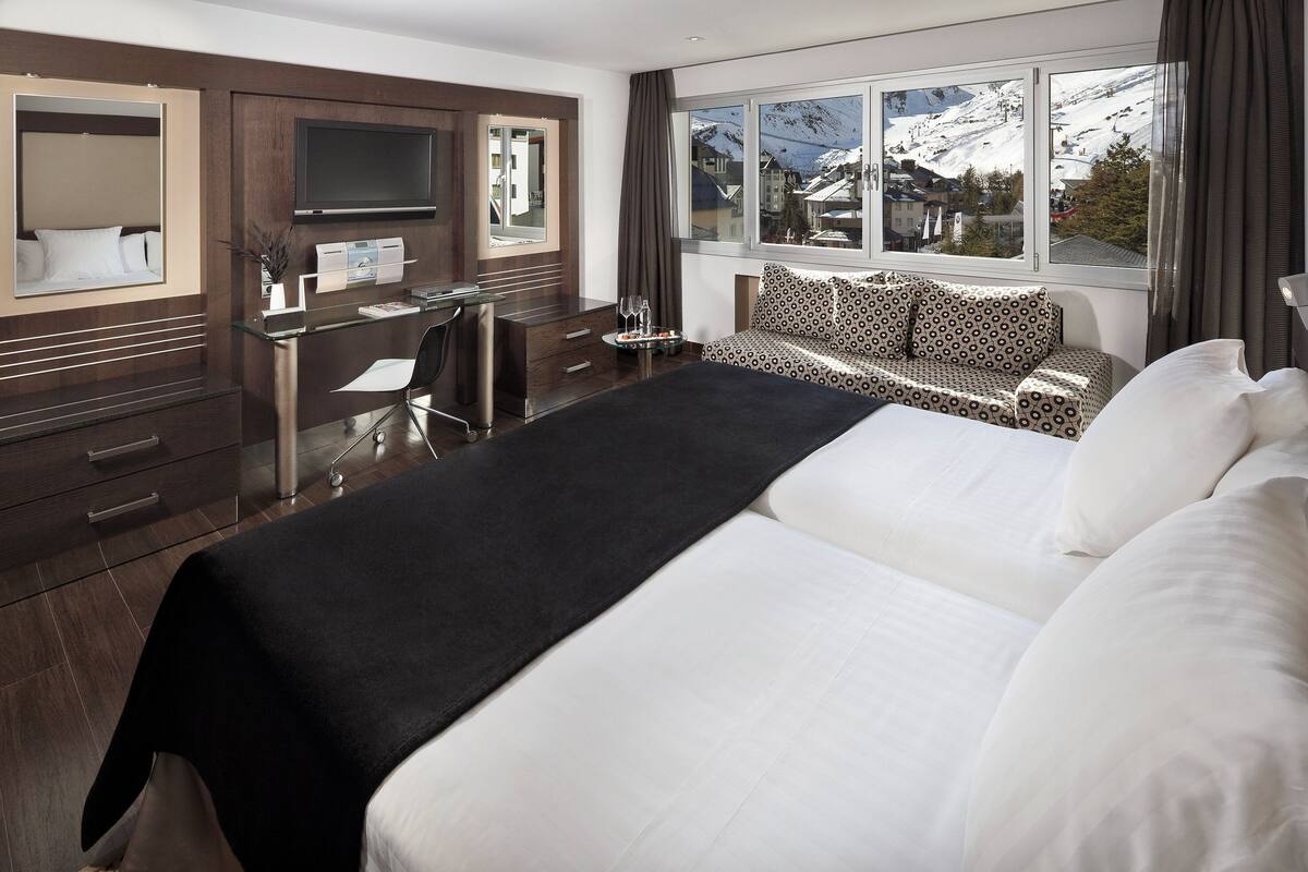 Habitación de hotel con una cama grande, un escritorio con silla, televisión y ventana con vista a la montaña.