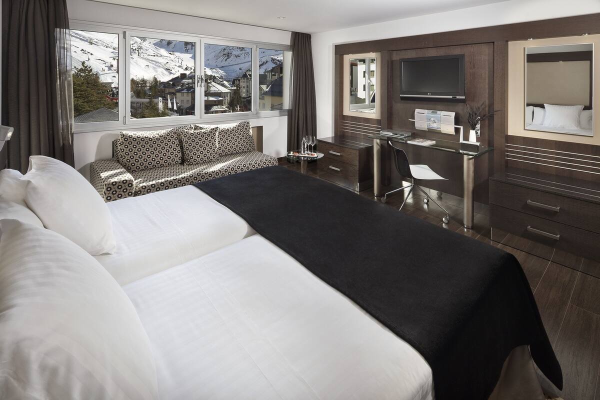 Habitación de hotel con una cama grande, un escritorio, una silla, un televisor y vistas a las montañas.