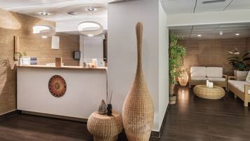 Un área de recepción con un mostrador de madera, dos grandes jarrones tejidos y una zona de estar con sofá y sillones.