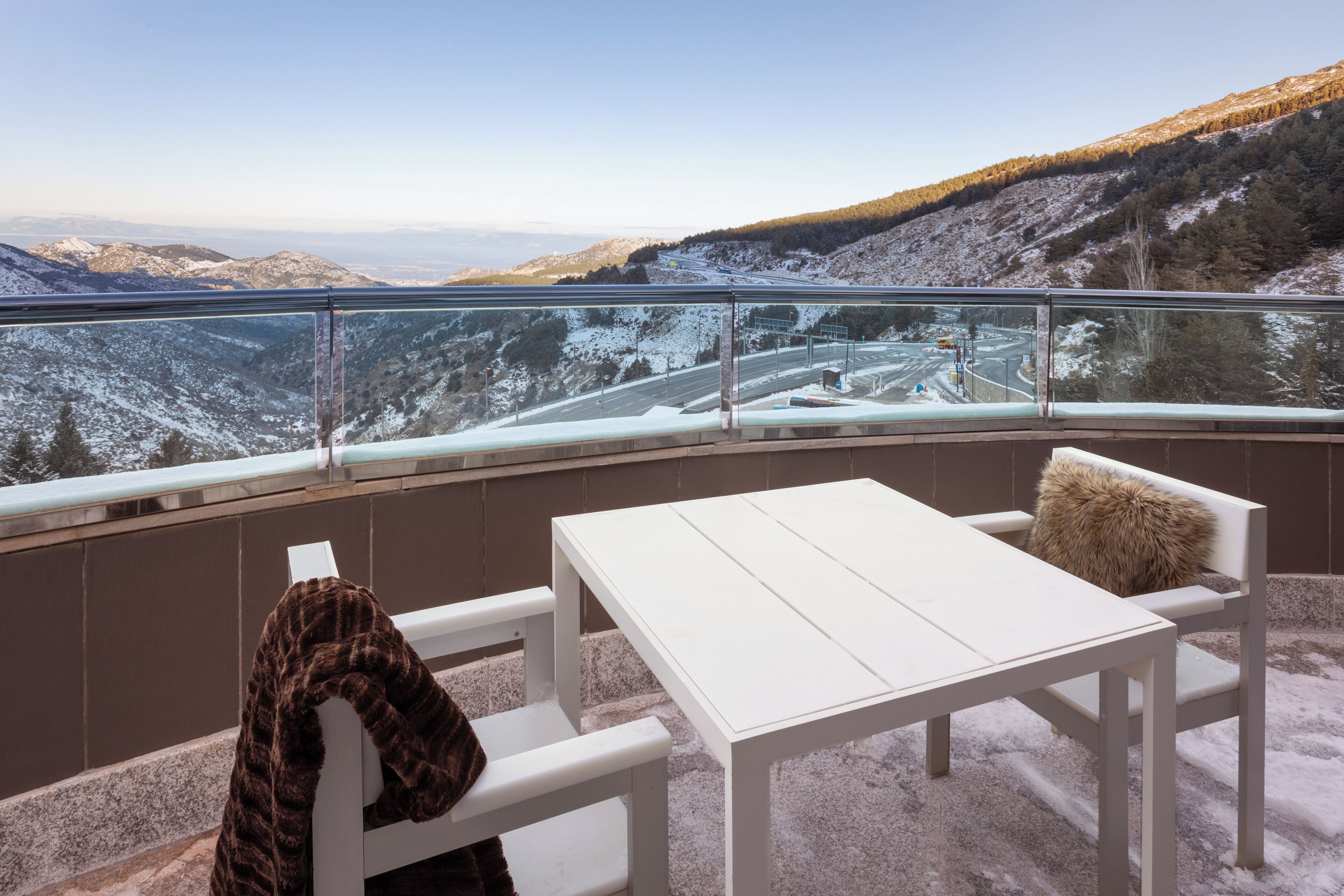 A balcony with a white table and bench, overlooking a snowy mountainous landscape.