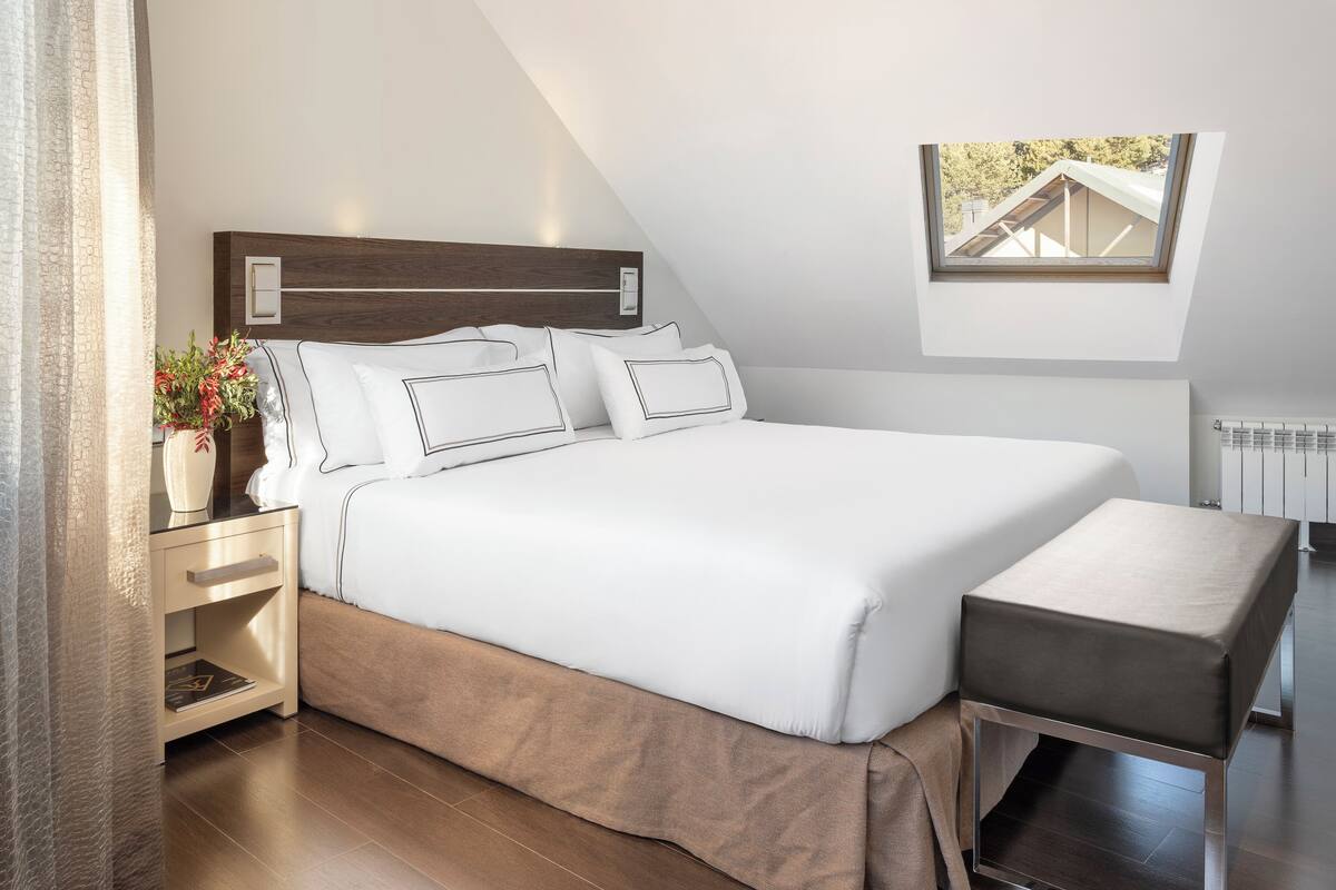 Un dormitorio moderno con una cama grande, mesitas de noche, un banco y un tragaluz.
