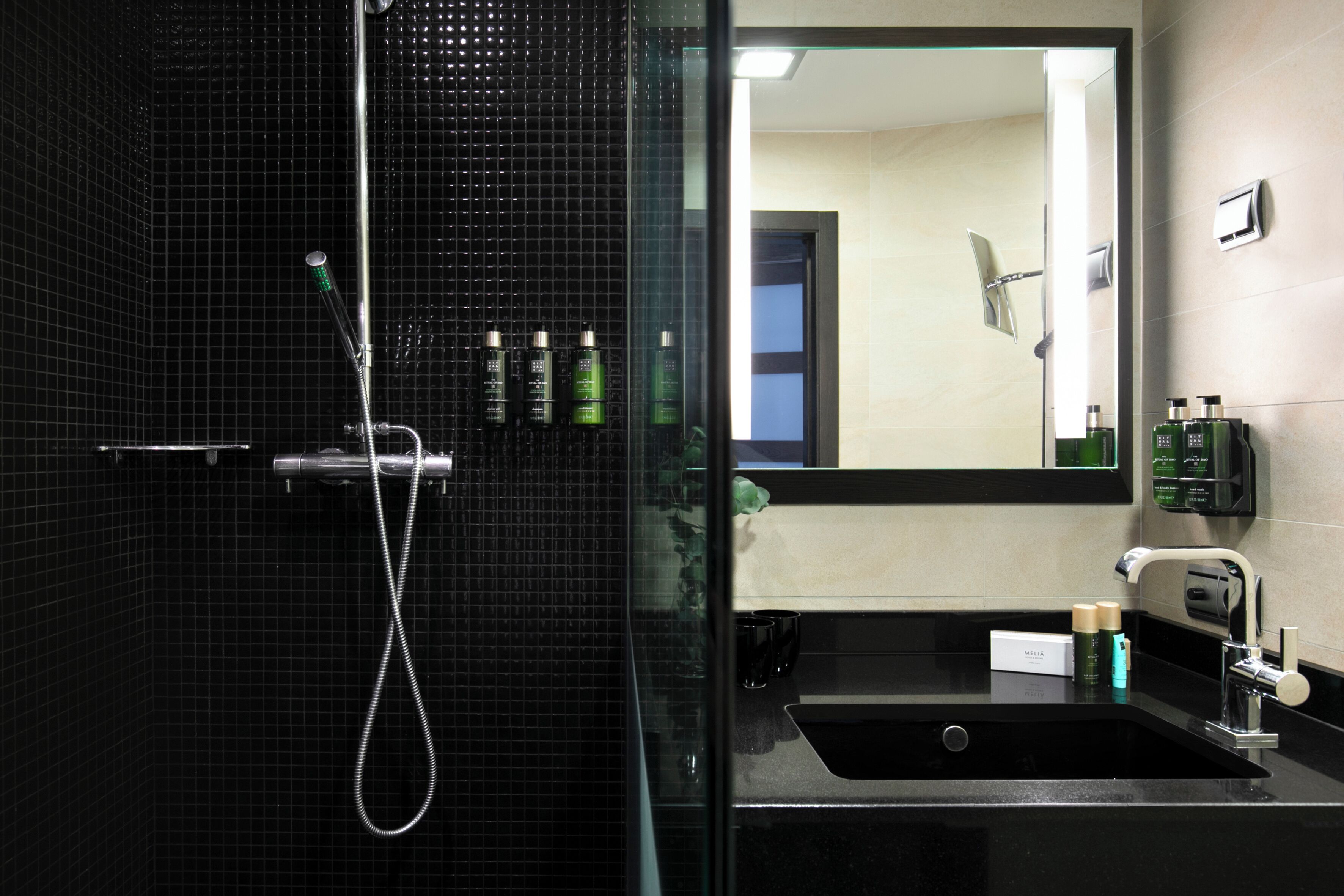 A modern bathroom with a glass-enclosed shower, a black sink, and a mirror reflecting the room.