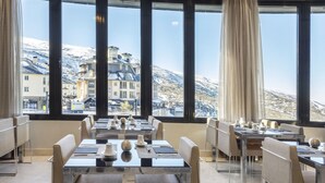 A restaurant with tables set for dining, large windows offering a view of snow-covered mountains and buildings. - Melia Sol Y Nieve (Monachil)