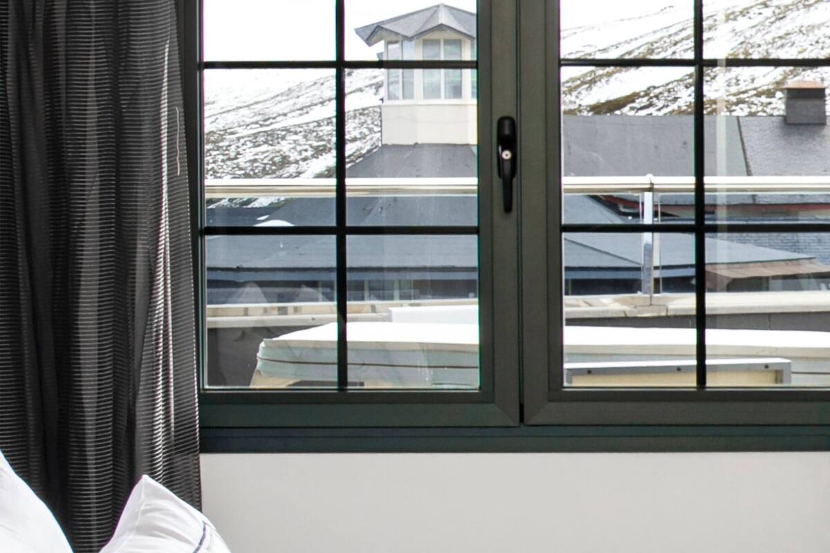 Una habitación con una cama, un ventanal con vistas a edificios y nieve, y una cortina.