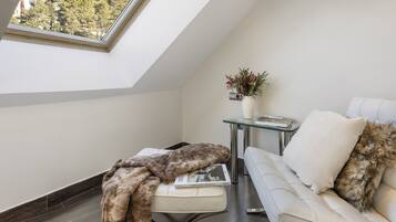 A modern loft bedroom with a skylight, a white sofa, a glass coffee table, and a decorative vase.