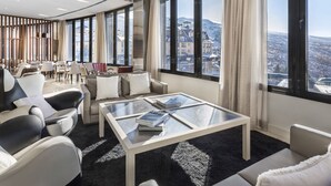 A modern hotel room with a large glass table, multiple seating options, and a panoramic city view. - Melia Sol Y Nieve (Monachil)