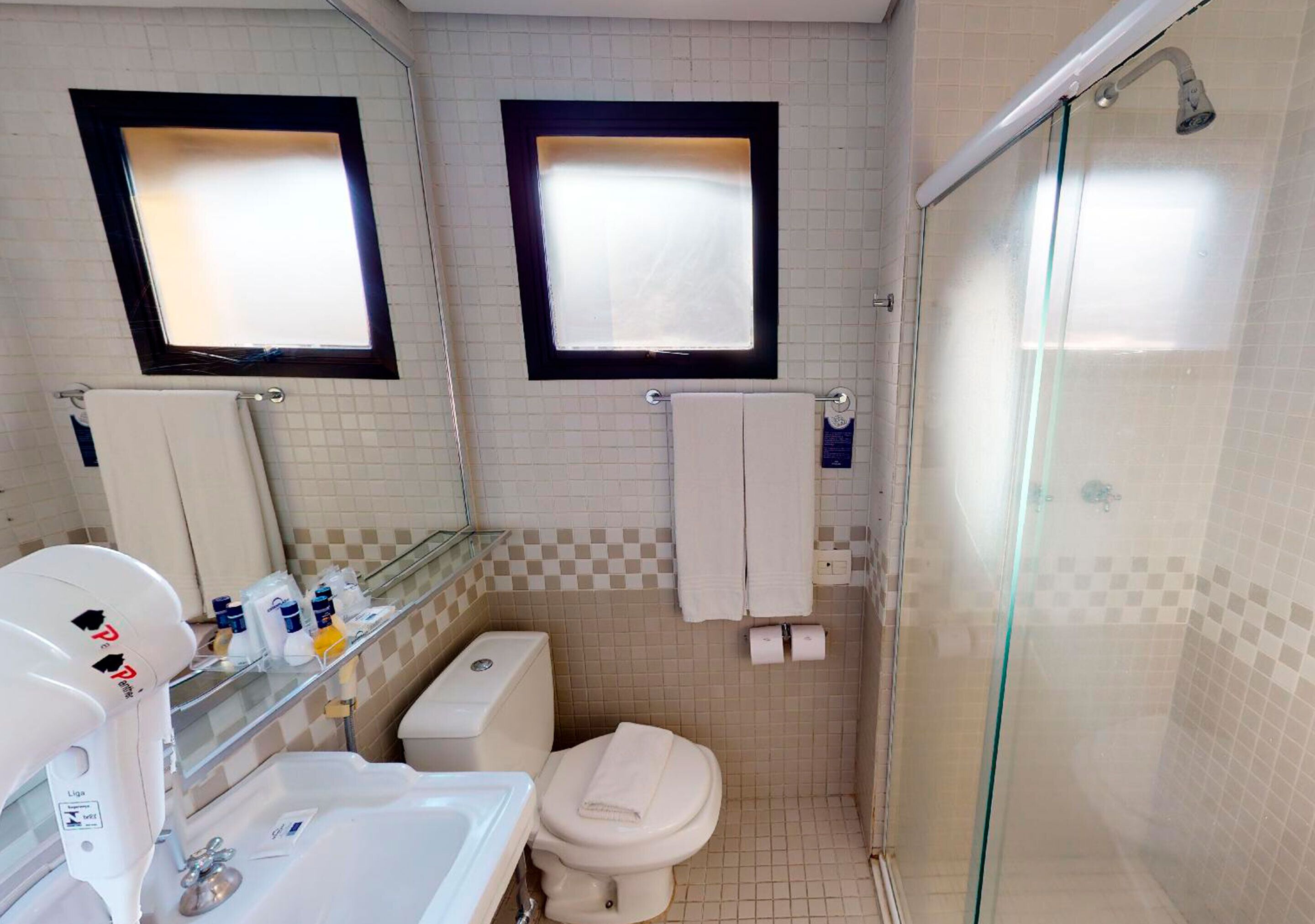 A bathroom with a toilet, sink, and shower. There are two mirrors above the mirrors, and a glass shower door.