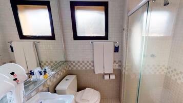 A bathroom with a toilet, sink, and shower. There are two mirrors above the mirrors, and a glass shower door.